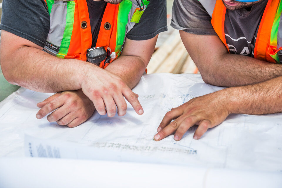 Mains désignant un plan déplié sur un établi